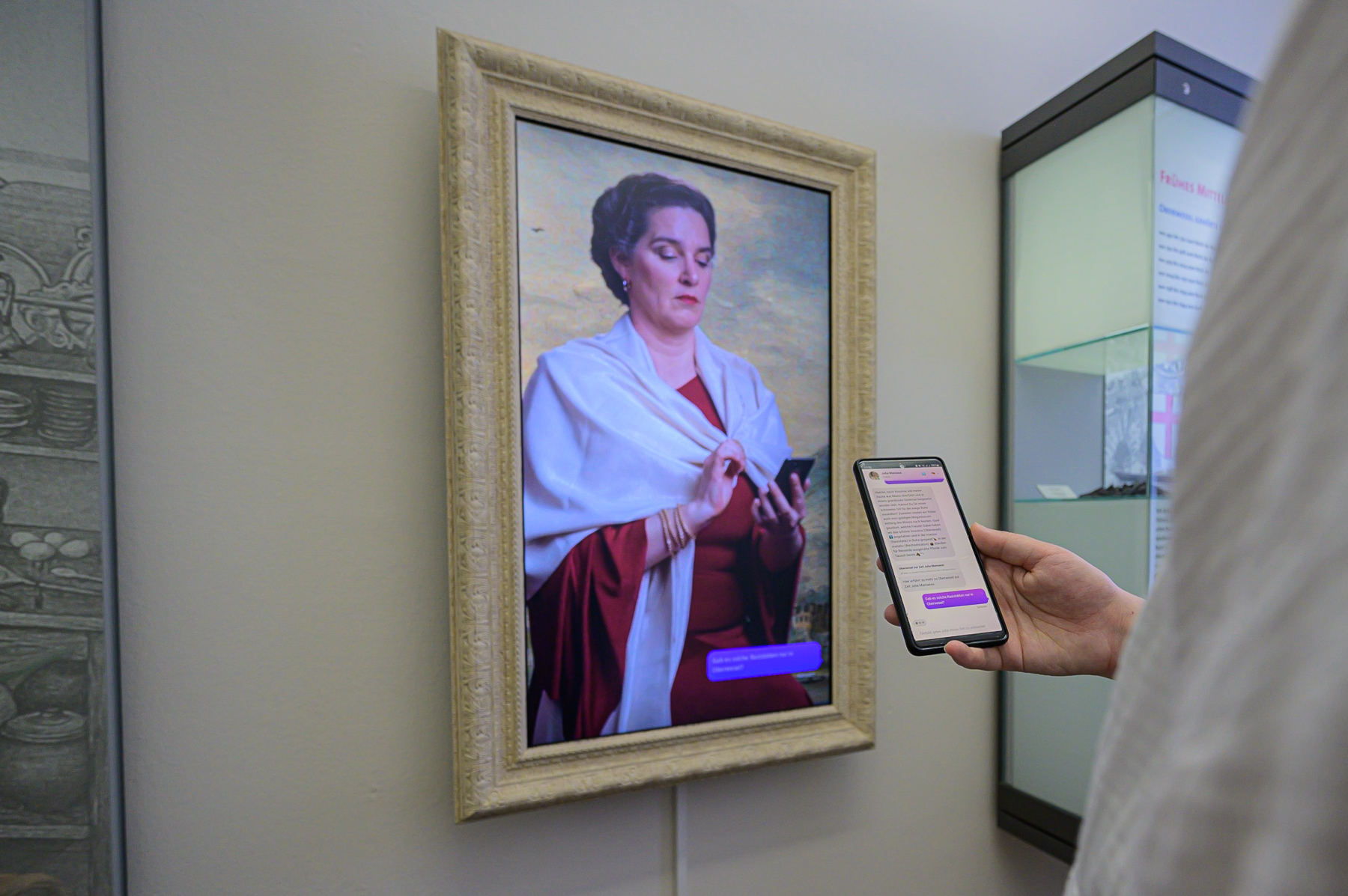 a picture of a well dressed woman with smartphone inside of a picture frame and a person staying in front of the portrait showing a chat